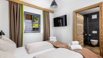 Une chambre d’hôtel avec un lit, une fenêtre avec des rideaux, une télévision et une salle de bain visible à travers une porte ouverte.