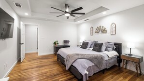 Een moderne slaapkamer met een bed, nachtkastjes, een plafondventilator en decoratieve wandkunst.