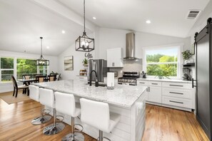 A modern kitchen with a large island, white cabinetry, stainless steel appliances, and a view of greenery outside. - Charming Country House   (Dacula)