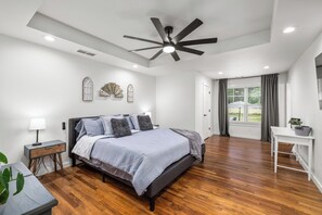 Une chambre à coucher avec un lit, un bureau, un ventilateur de plafond et une fenêtre avec des rideaux.