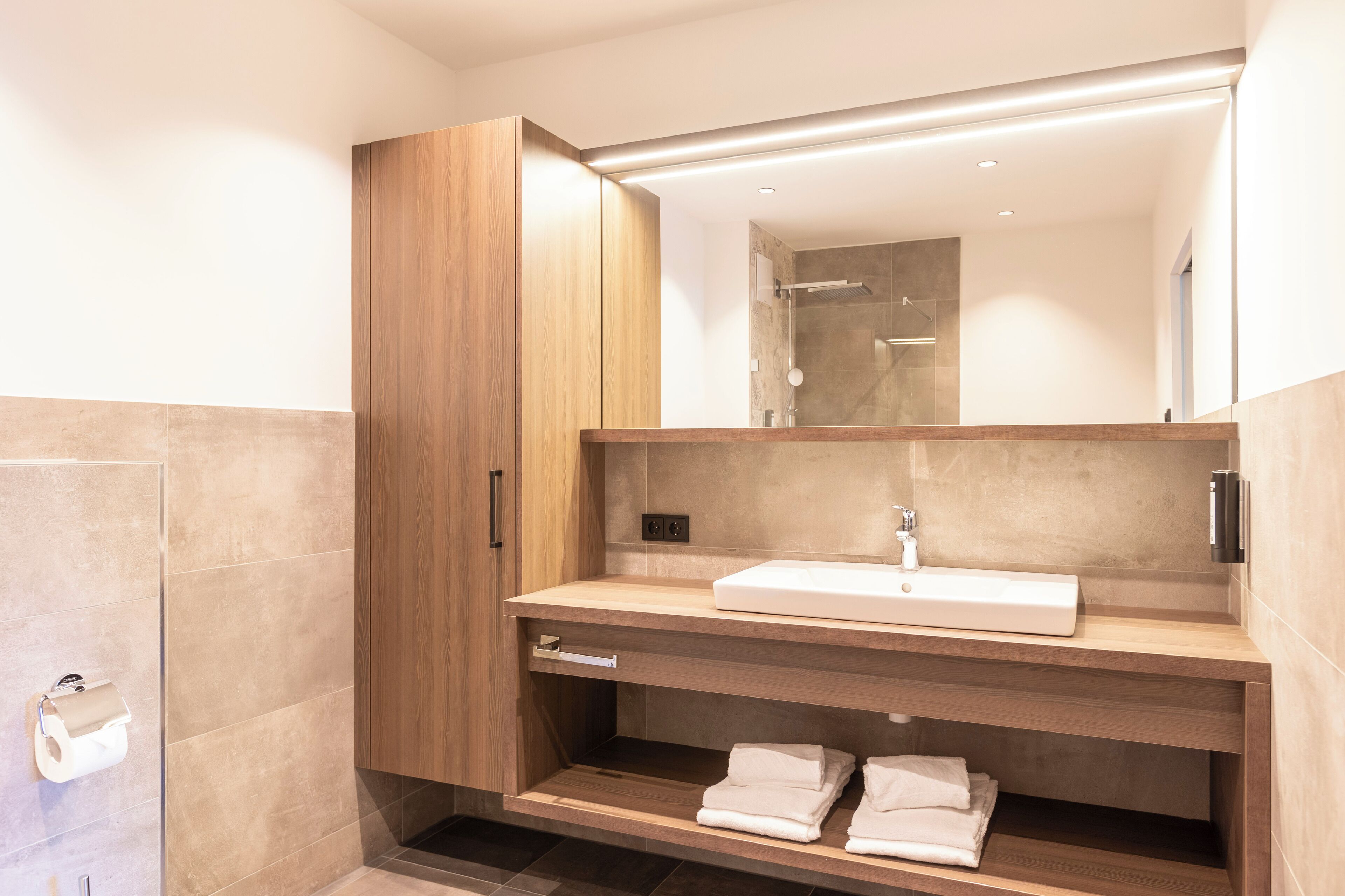 Un baño moderno con un tocador de madera, un espejo grande y una ducha integrada.