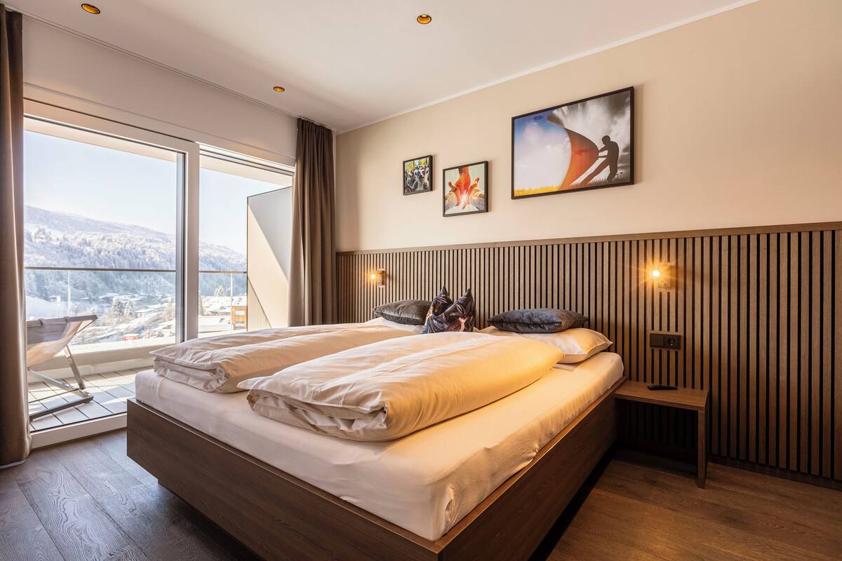 Moderni hotellihuone, jossa on suuri sänky, näkymä lumiseen maisemaan ja puinen sängynpääty.