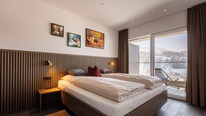 A modern bedroom with a large bed, a bedside table, a wall-mounted lamp, and a window with a view of a snowy landscape.