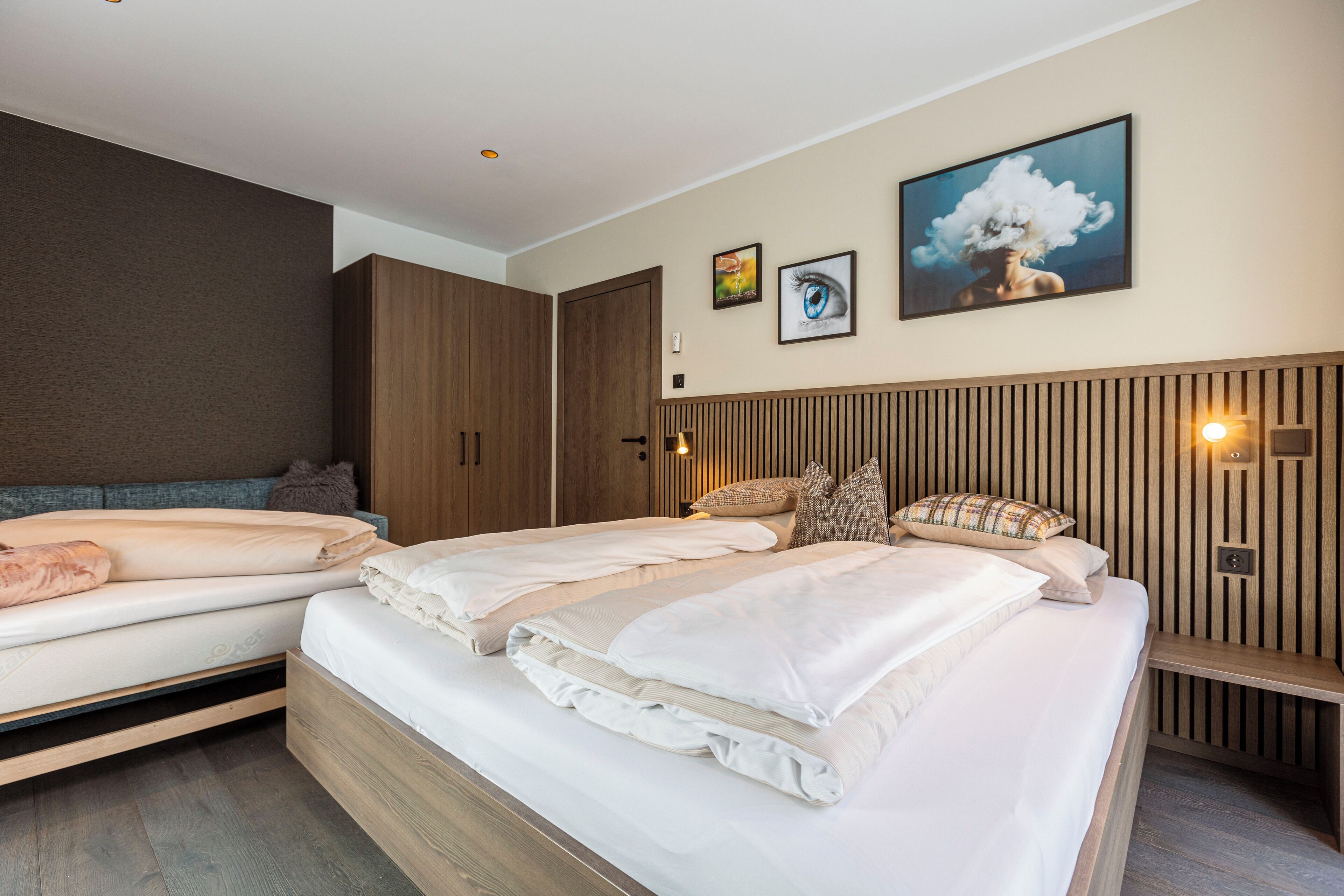 A modern bedroom with two beds, wooden headboard, and wall-mounted artwork.