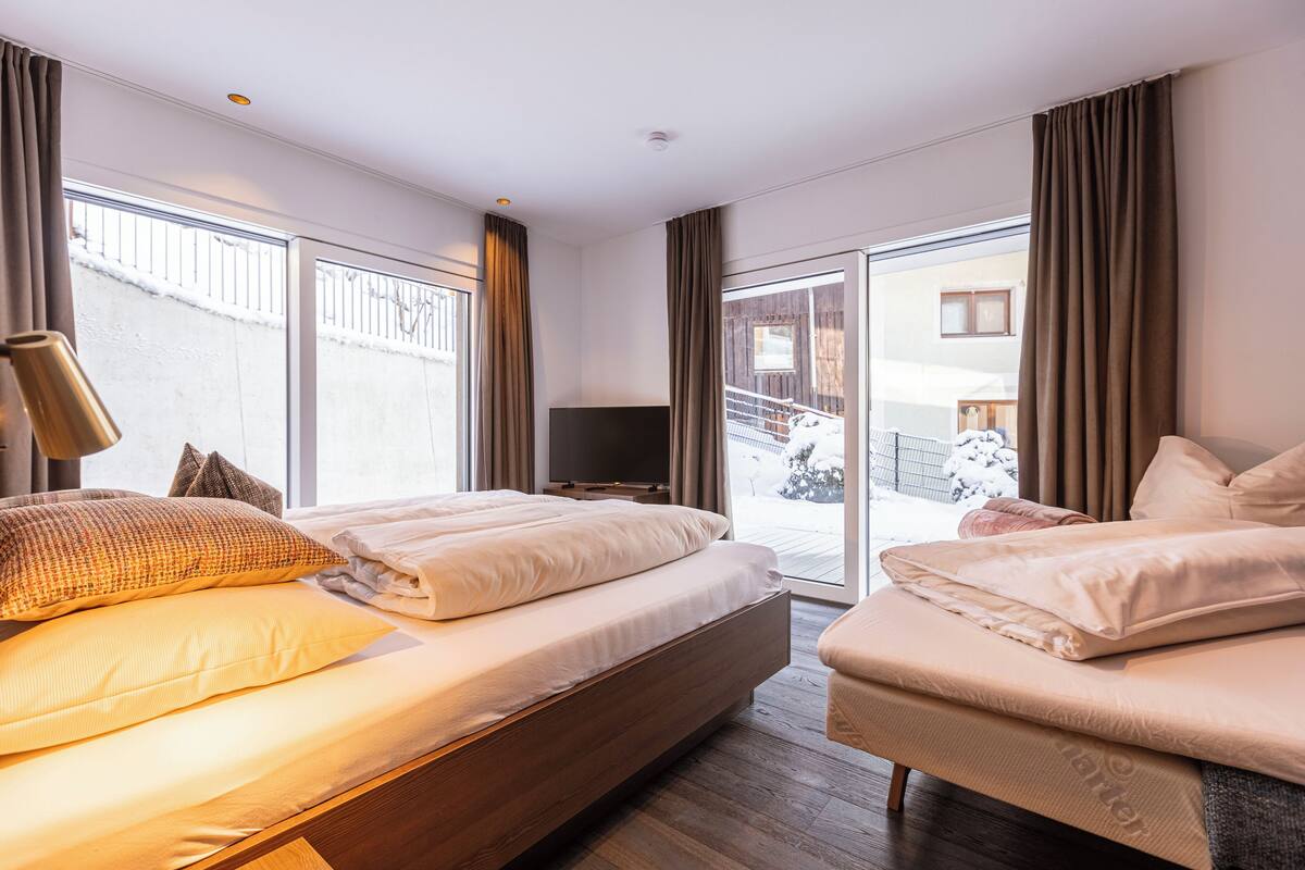 Moderni hotellihuone, jossa on suuri sänky, pienempi sänky, televisio ja liukuovet, jotka johtavat parvekkeelle.
