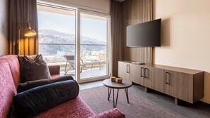 A modern living room with a sofa, a flat-screen TV, a wooden cabinet, and a view of a snowy mountain.