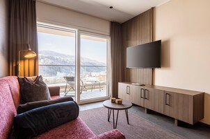 Una sala moderna con un sofá, un televisor de pantalla plana, un mueble de madera y vistas a una montaña nevada.
