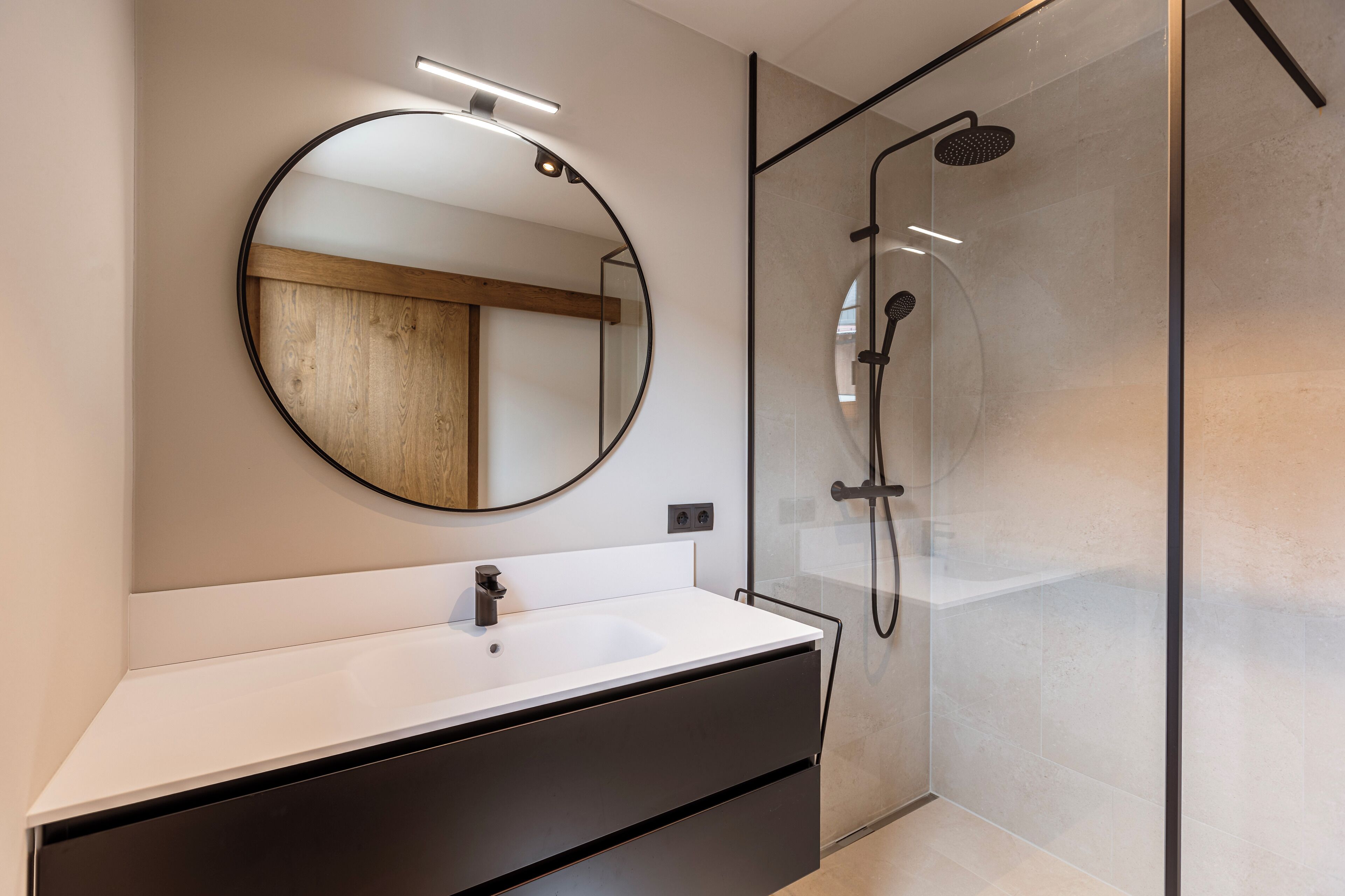 A modern bathroom with a round mirror, a white sink, and a glass-enclosed shower.