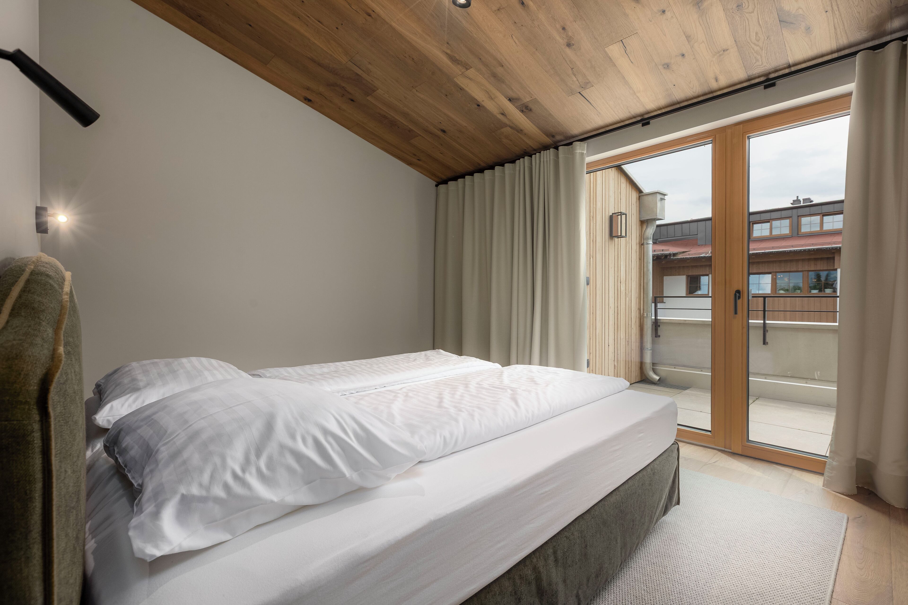 Un dormitorio con techo de madera, una cama con ropa blanca, un patio con puerta corrediza de vidrio y una toalla en el suelo.