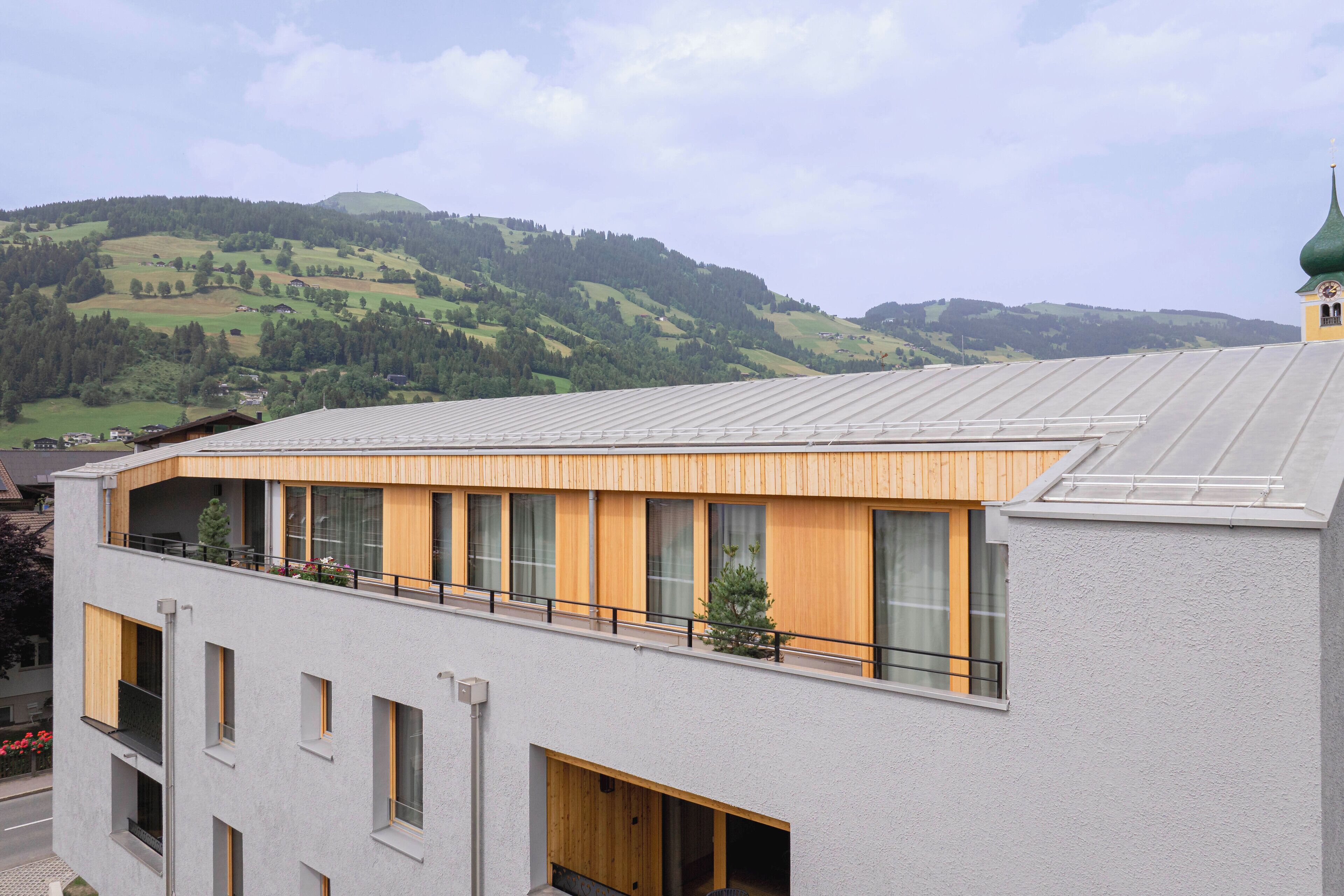 Un edificio moderno con techo plano, ventanas grandes y un balcón con vistas a un paisaje montañoso.