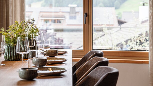 Une table à manger avec des chaises, une fenêtre donnant sur les montagnes et un vase rempli de fleurs.
