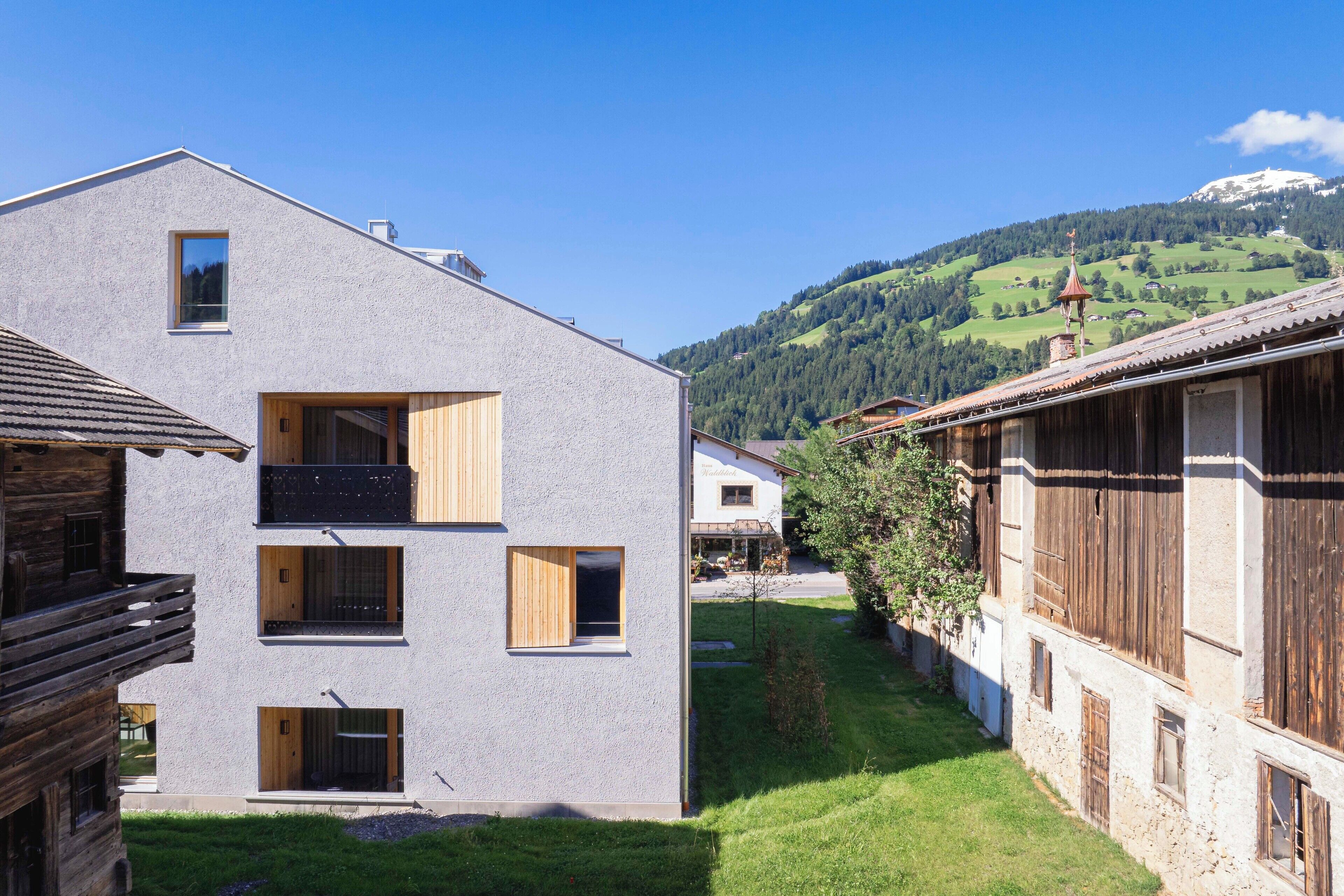 A modern building with a sloped roof, wooden balconies, and a view of a green hillside.