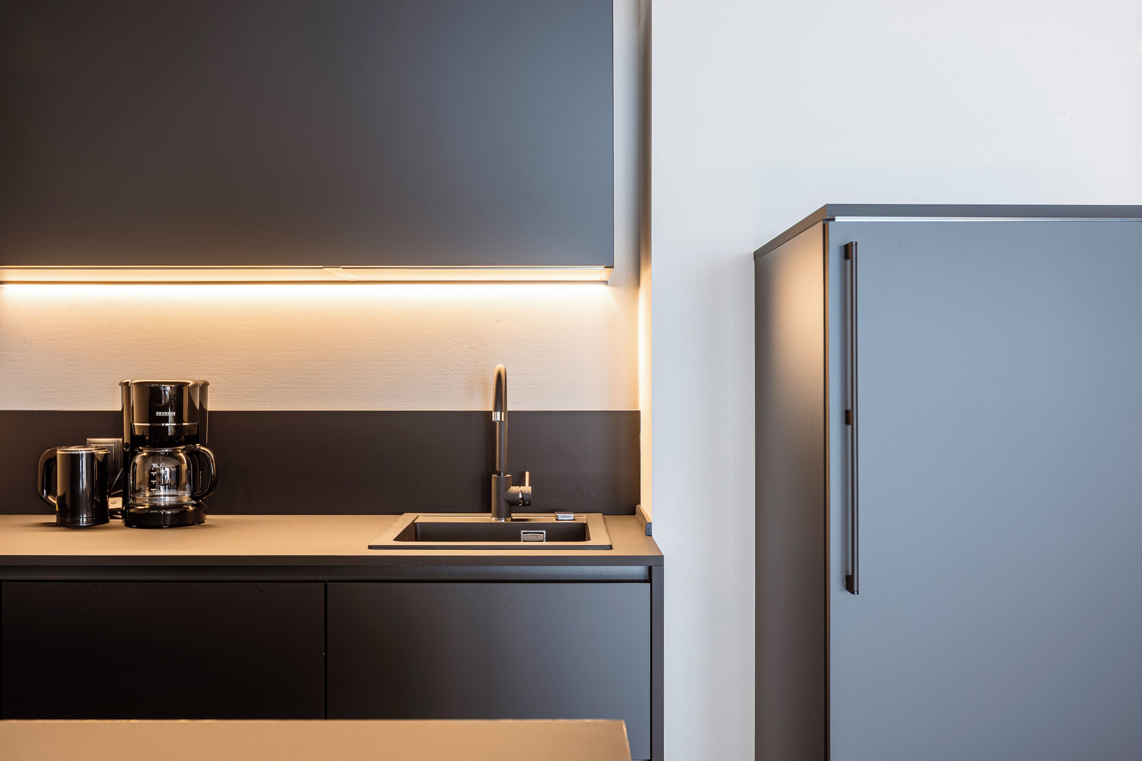 Una cocina moderna con cafetera integrada, un lavamanos y un refrigerador.