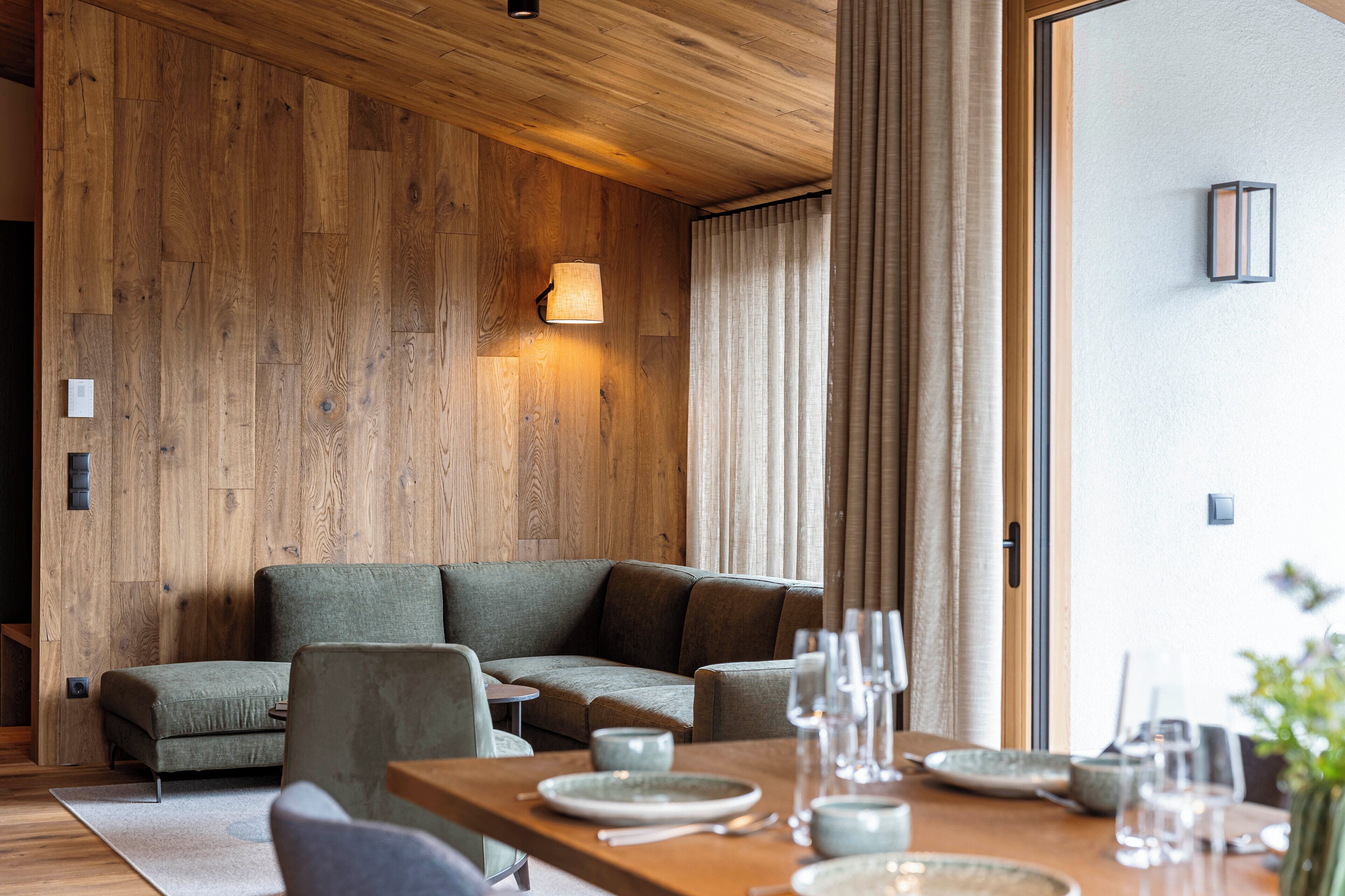 Un interior moderno con una pared de madera, un sofá, una mesa de comedor con platos y vasos, y una lámpara.