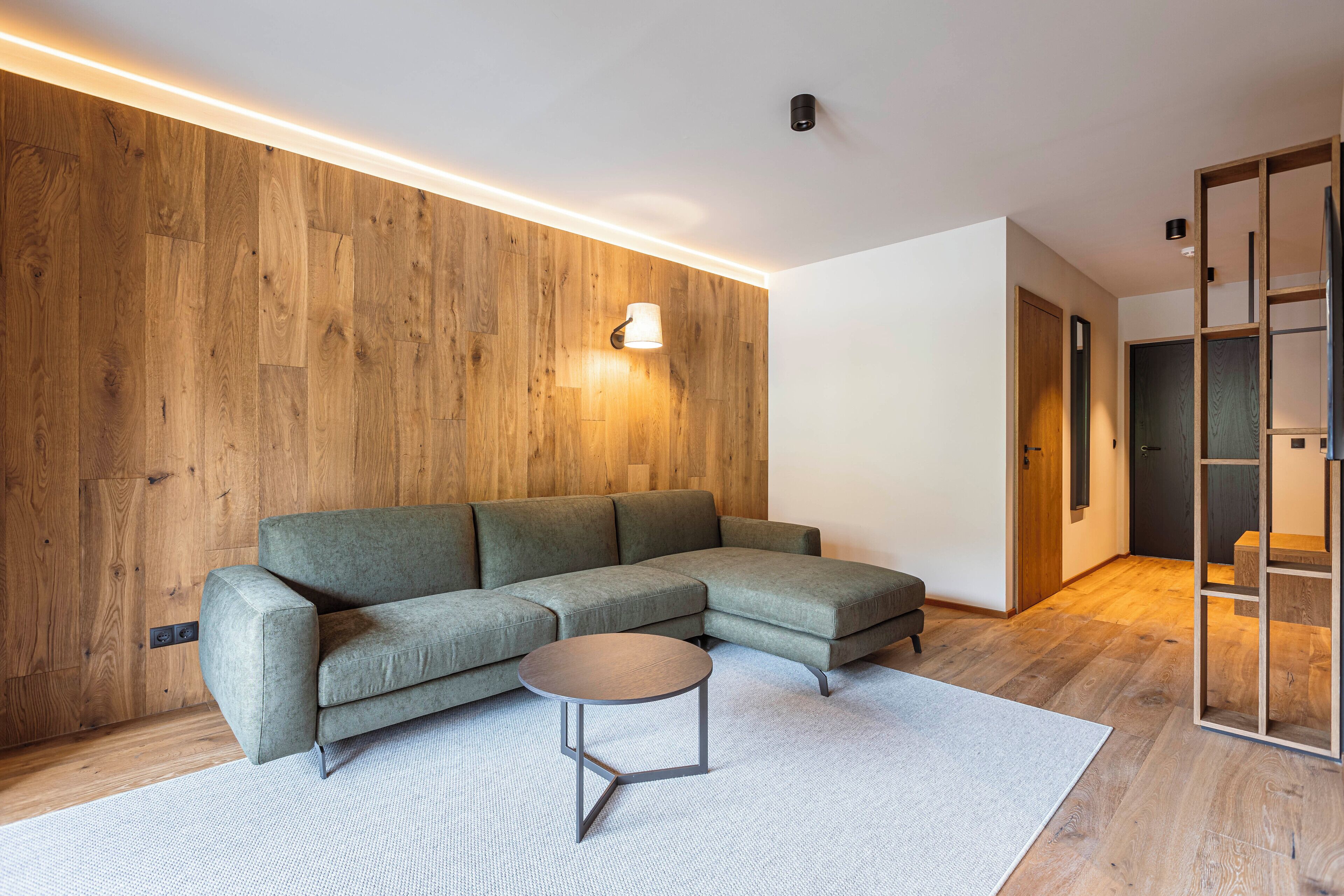 Un salon moderne avec un canapé d’angle, une table basse ronde et un mur décoratif en bois.