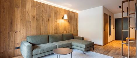 Un salon moderne avec un canapé d’angle, une table basse ronde et un mur décoratif en bois.