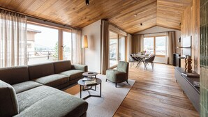 Un vaste espace de vie doté d’un plafond en bois, de grandes fenêtres, d’un canapé, d’une table basse et d’un coin repas.