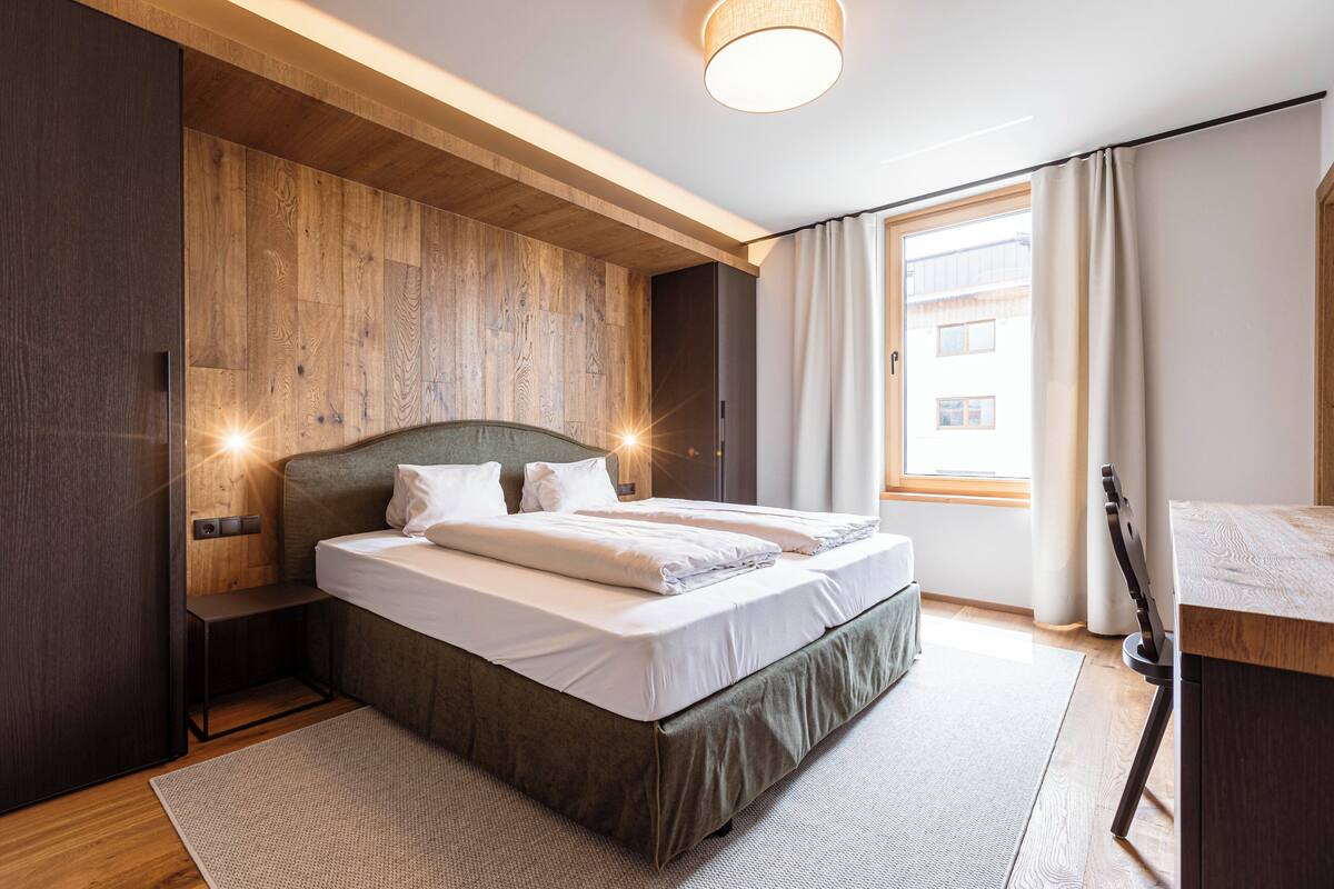 Ein modernes Schlafzimmer mit einem Holzkopfteil, einem Bett mit weißen Laken, einem Nachttisch und einem Schreibtisch mit Stuhl.