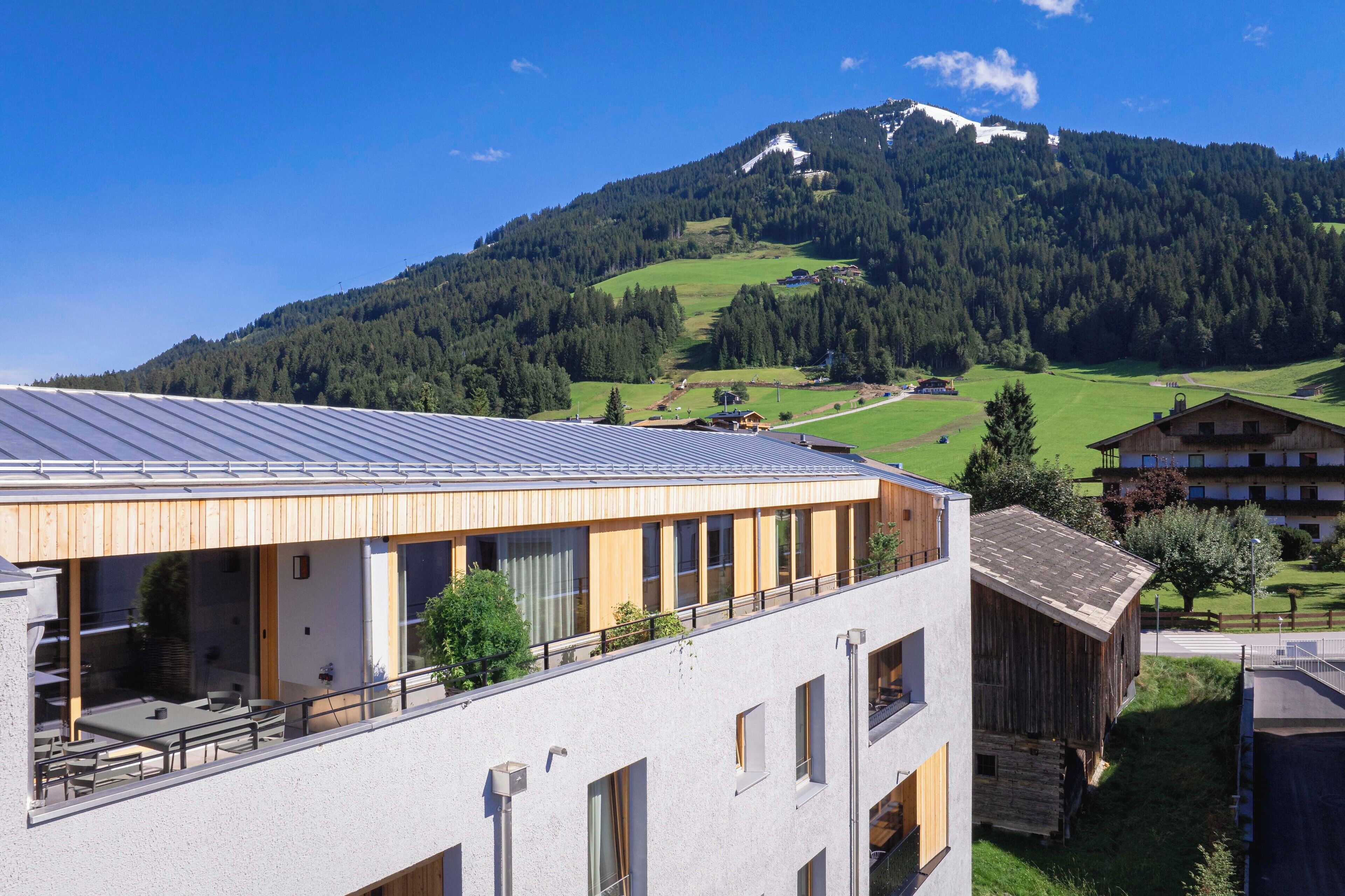 A modern building with a flat roof and large windows, overlooking a green valley and a mountain.