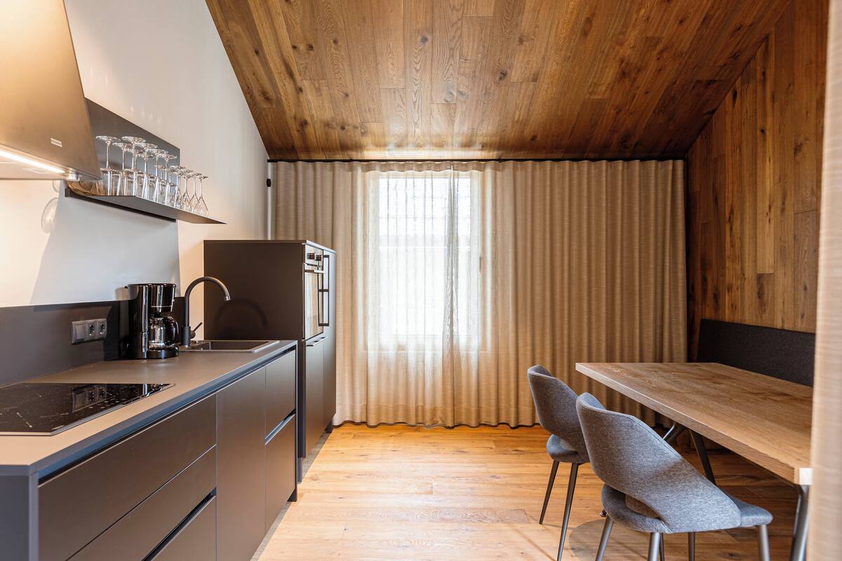 Eine moderne Küche mit Holzboden, integriertem Herd, einer Kaffeemaschine und einem Essbereich mit Tisch und Stühlen.