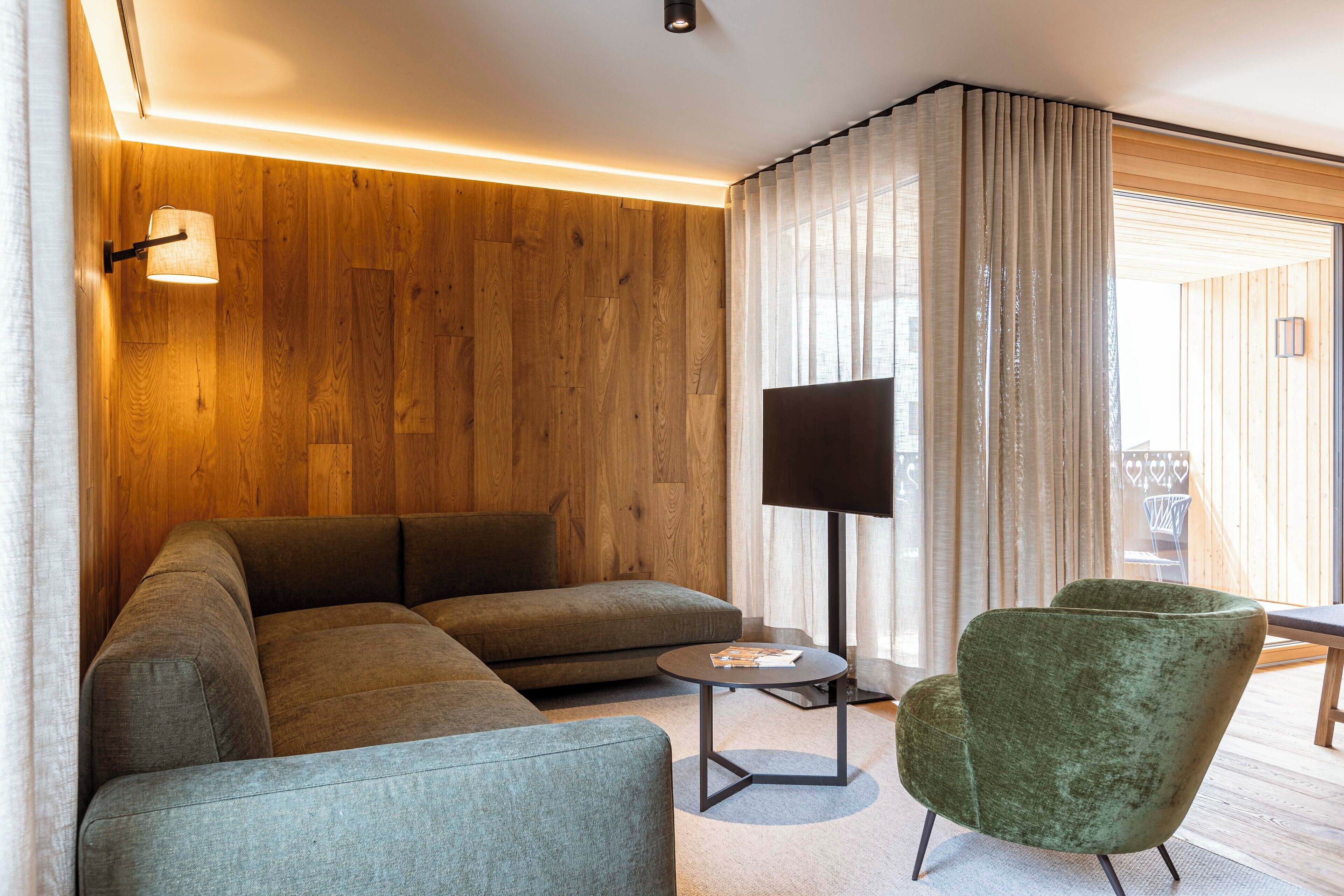 Un salon moderne avec un canapé d’angle, une table basse ronde et un fauteuil vert.