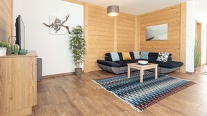 A modern living room with a wooden wall, a black sofa, a wooden coffee table, and a colorful rug. - Naturpark Chalets Lambrecht (Sankt Lambrecht)