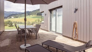 An outdoor patio with a table and chairs, a lounge chair, and a view of a green landscape. - Naturpark Chalets Lambrecht (Sankt Lambrecht)