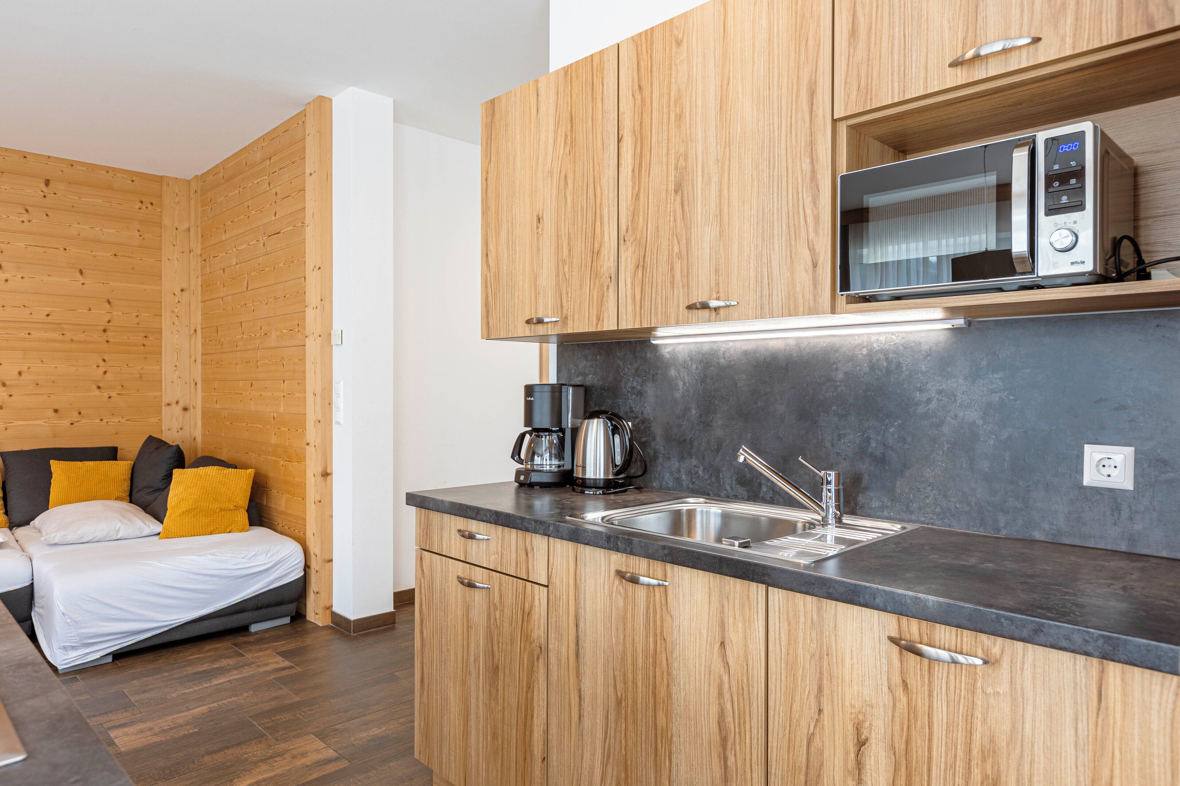 A compact kitchen with wooden cabinets, a microwave, a coffee maker, and a sink.