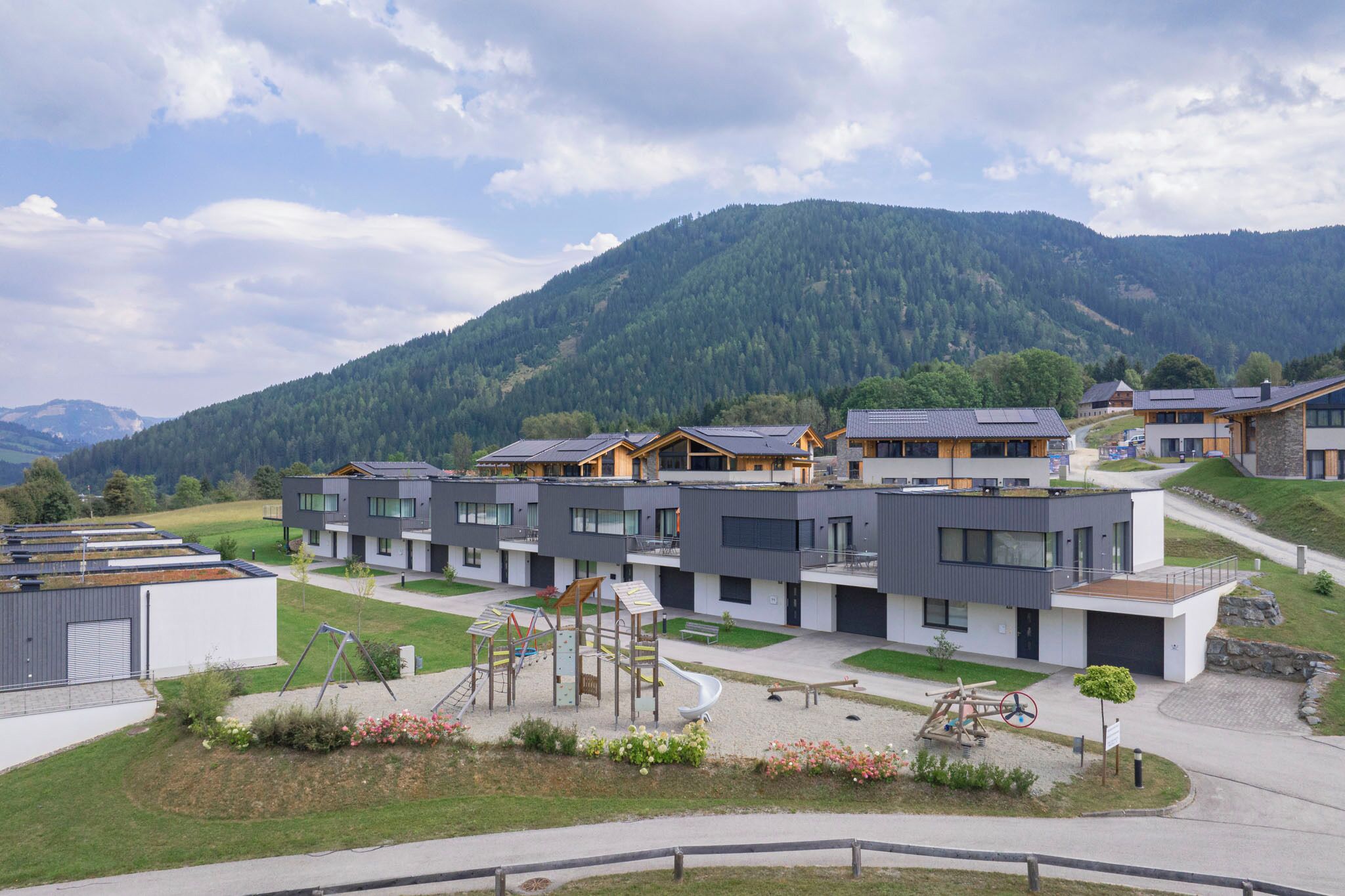 A modern residential complex with multiple houses, a playground, and a mountainous backdrop.