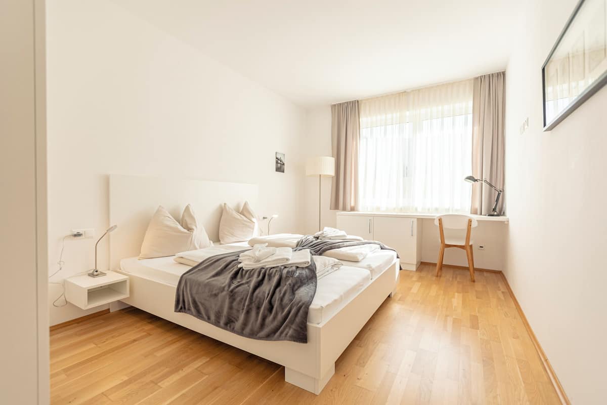 A modern bedroom with a white bed, a desk, and a chair.