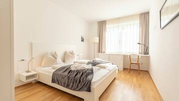 Un dormitorio moderno con una cama blanca, un escritorio y una silla.