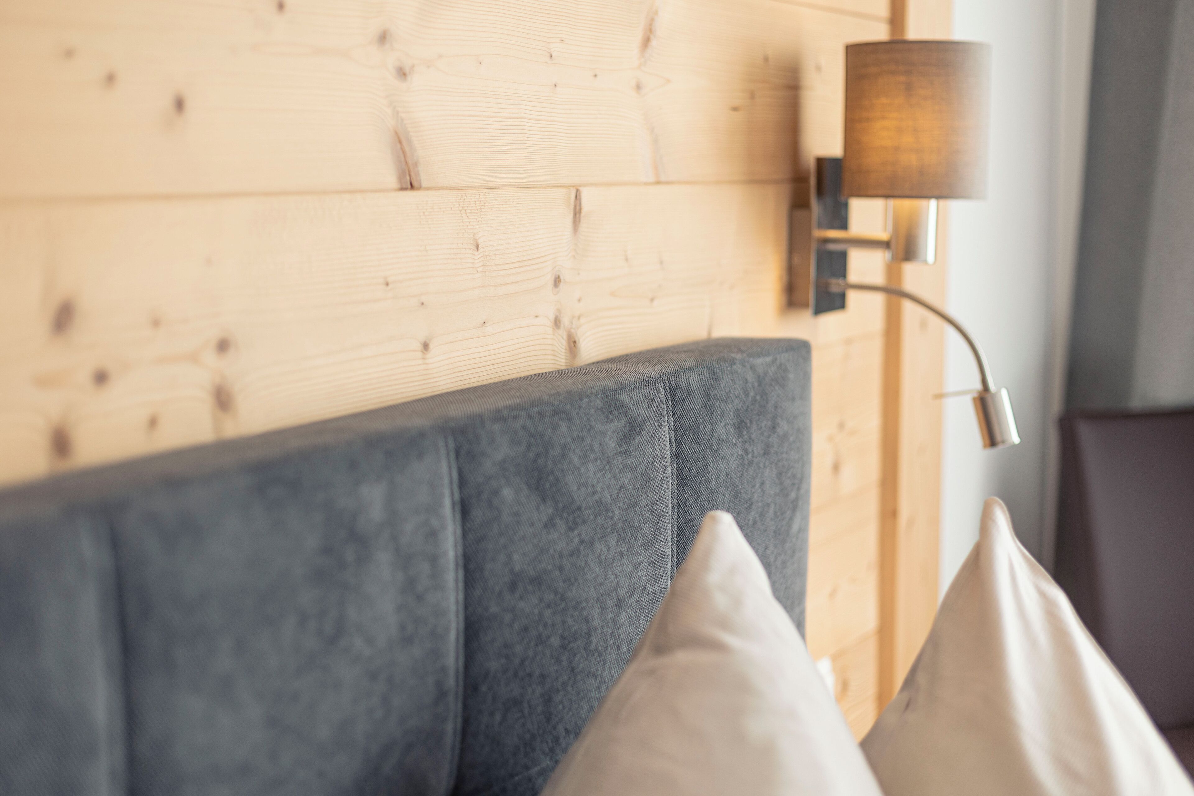 A modern living room with a grey sofa, wooden wall paneling, and a wall-mounted lamp.