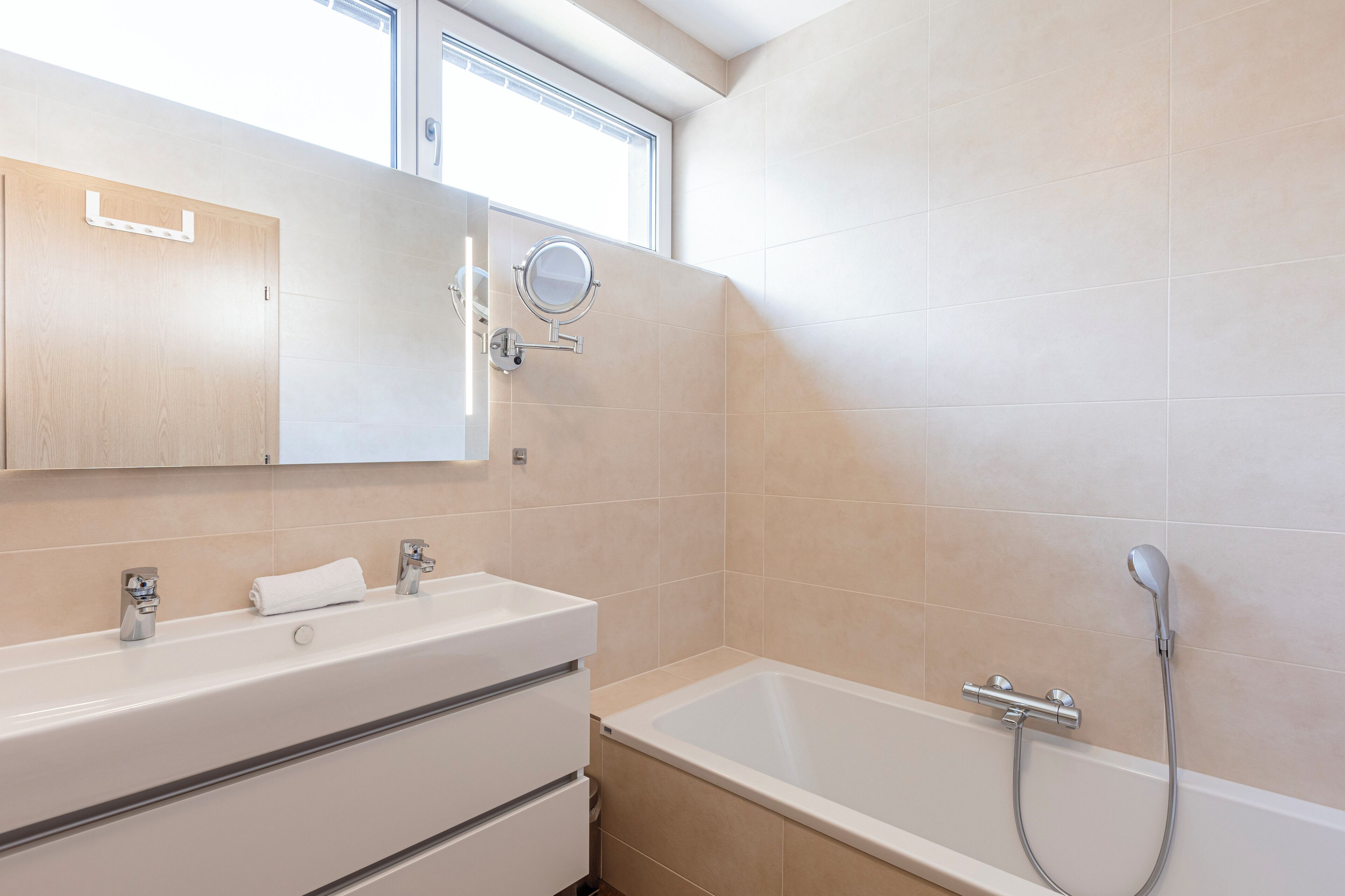 Une salle de bain moderne avec une baignoire, un meuble-lavabo avec un miroir et une fenêtre située au-dessus du miroir.