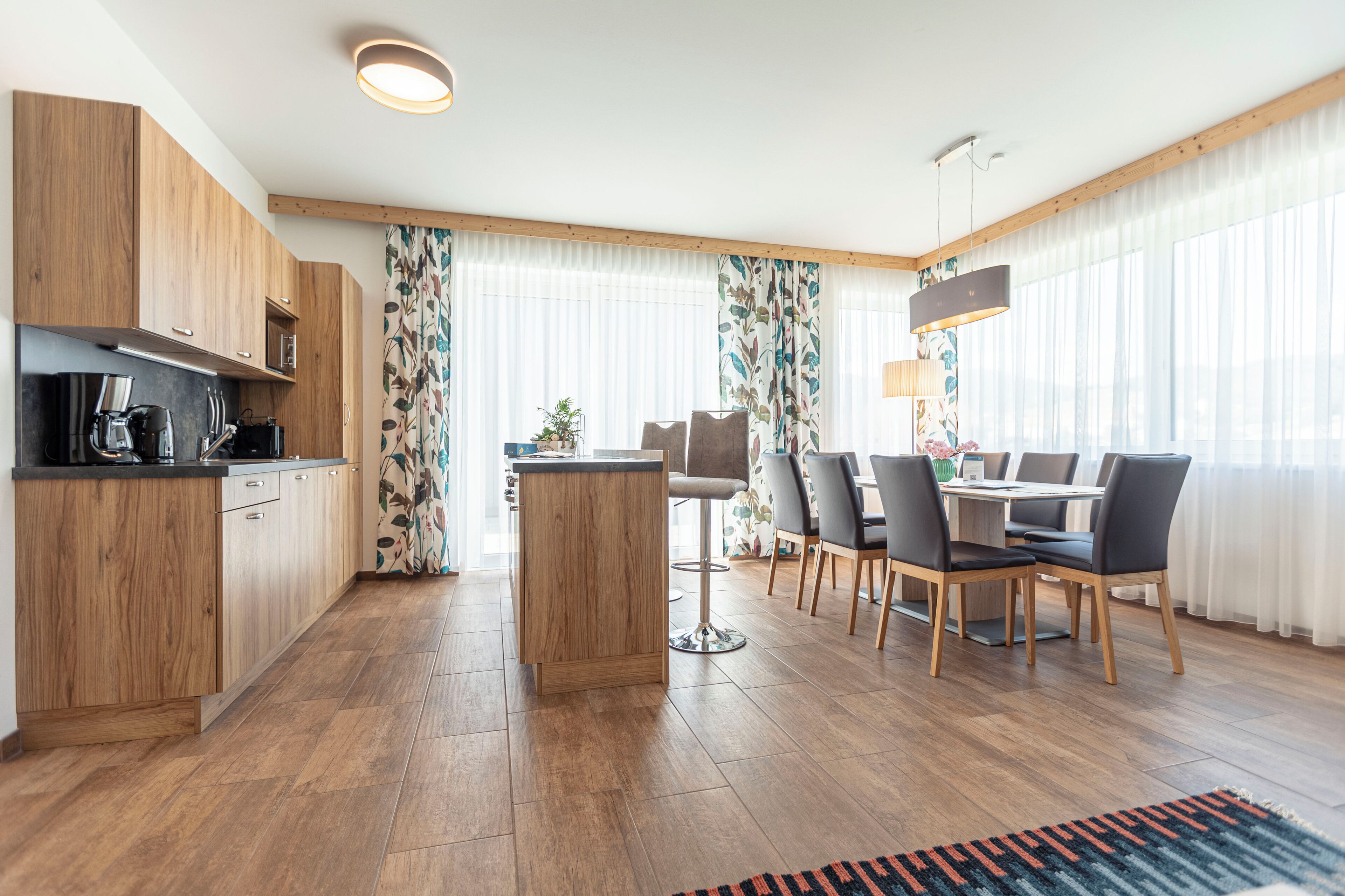 A modern kitchen with wooden cabinets, a central island, and a dining area with a table and chairs.