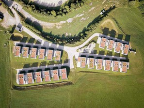 An aerial view of a residential complex with multiple buildings arranged in a U-shape, surrounded by green fields and trees. - Naturpark Chalets Lambrecht (Sankt Lambrecht)