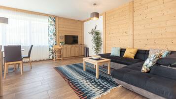 Ein modernes Wohnzimmer mit einem dunklen Sofa, Holzböden, einem Fernseher und einem Essbereich mit Stühlen und einem Tisch.