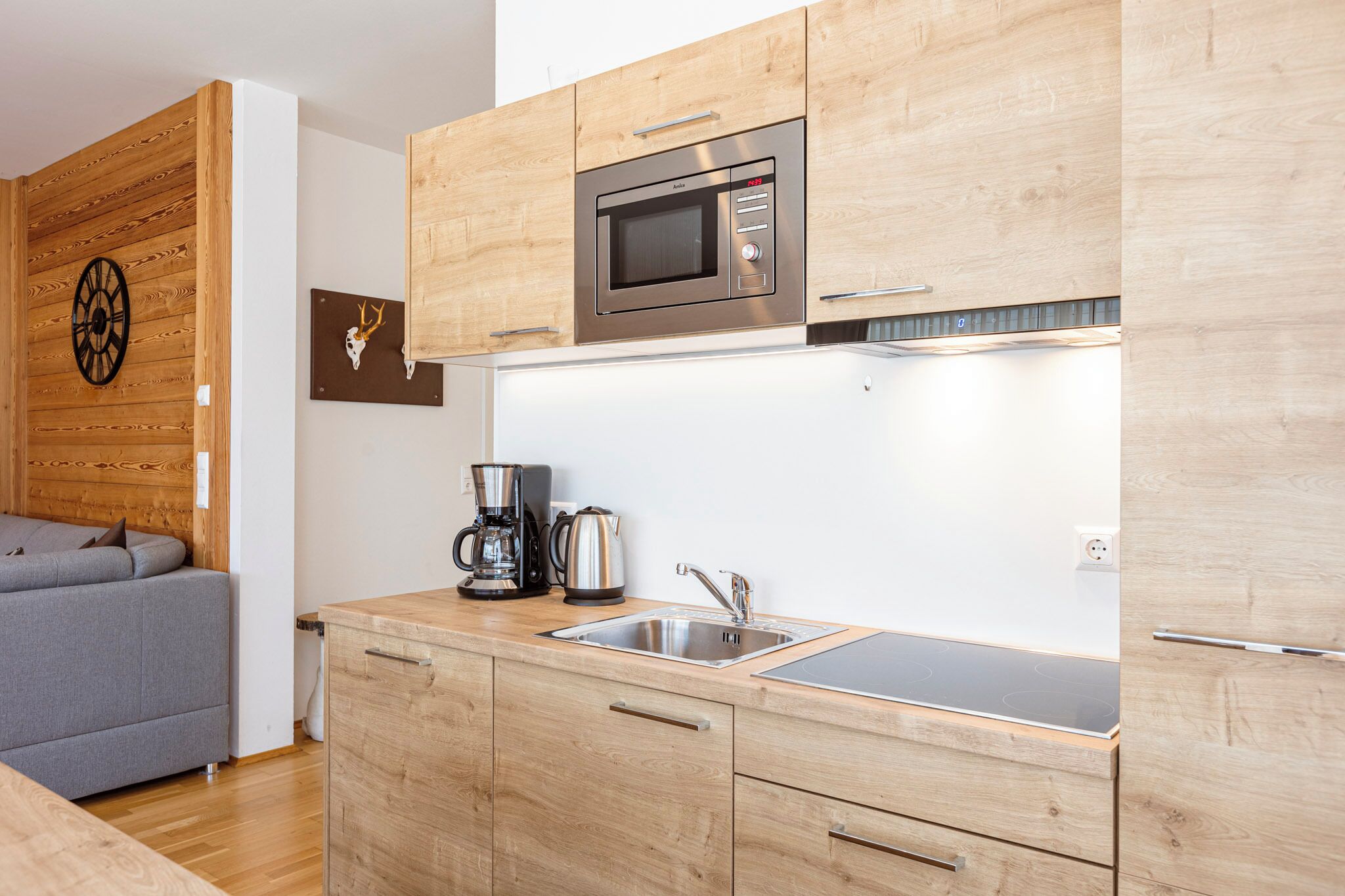 A modern kitchen with wooden cabinets, a built-in microwave, a coffee maker, and a sink.