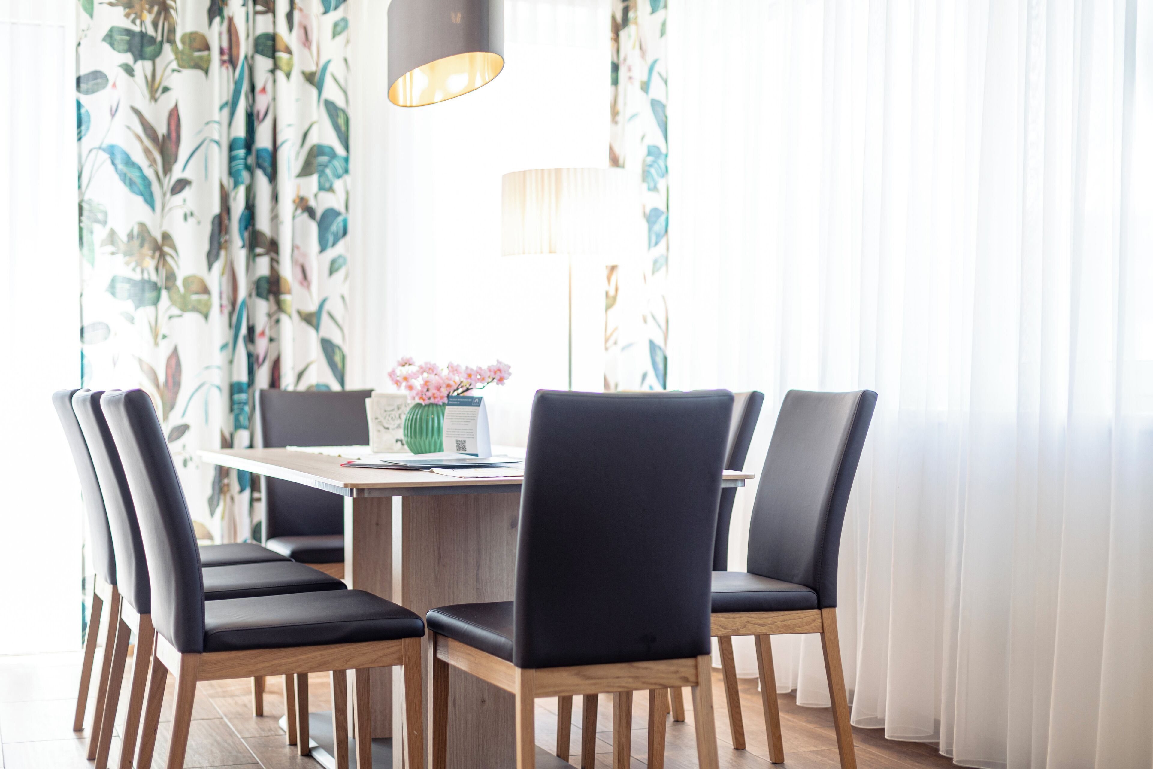 Un comedor con una mesa de madera y sillas negras, un jarrón con flores y una lámpara.