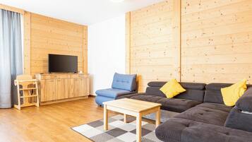 A modern living room with a wooden floor, a sofa set, a television, and a small wooden table.