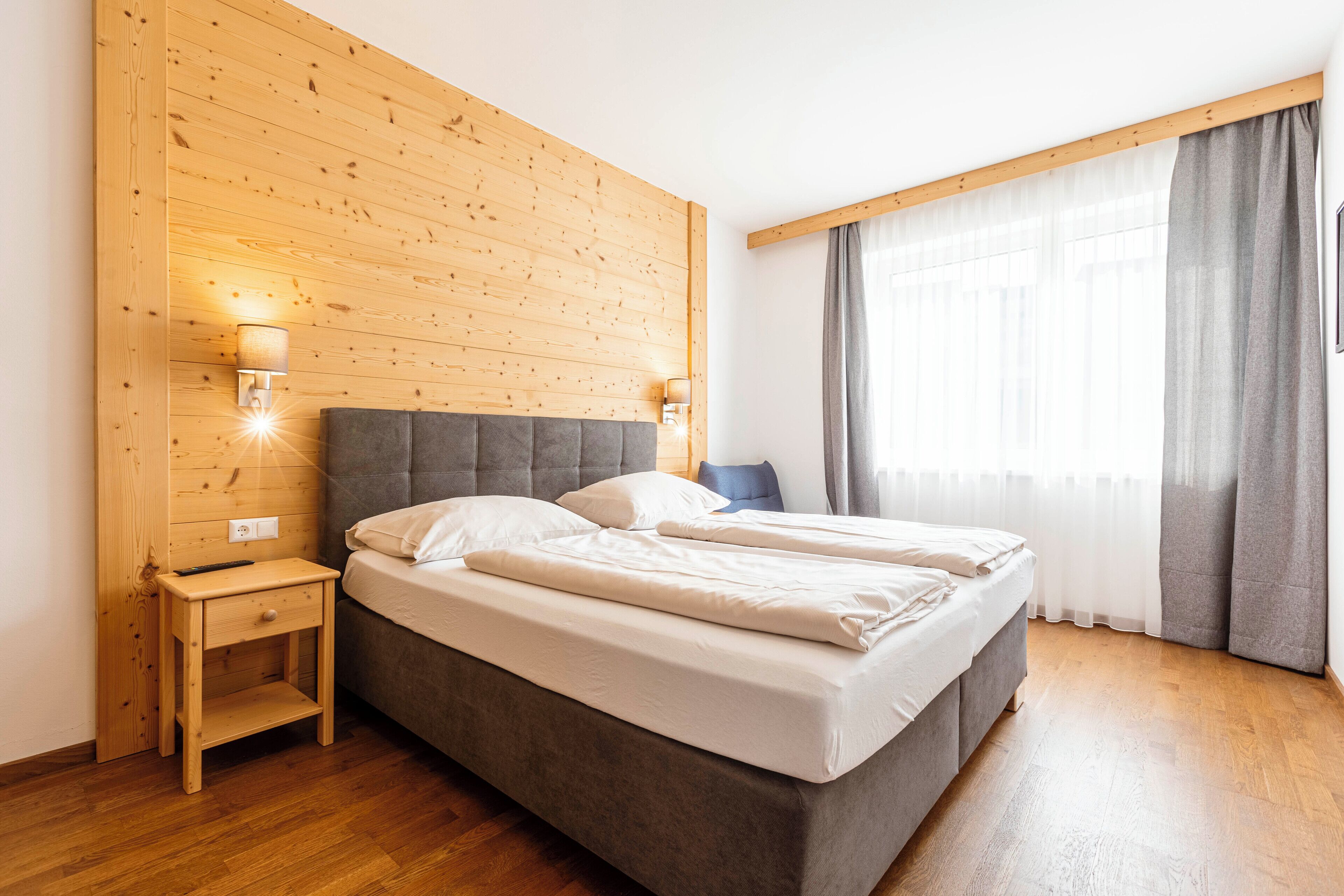 A double bed with a wooden headboard, a nightstand, and two wall-mounted lamps.