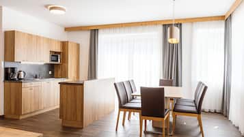 Eine moderne Küche mit Holzausstattung, einer Mikrowelle und einer Kaffeemaschine. Es gibt eine Essecke mit Tisch und Stühlen sowie ein großes Fenster mit Vorhängen.