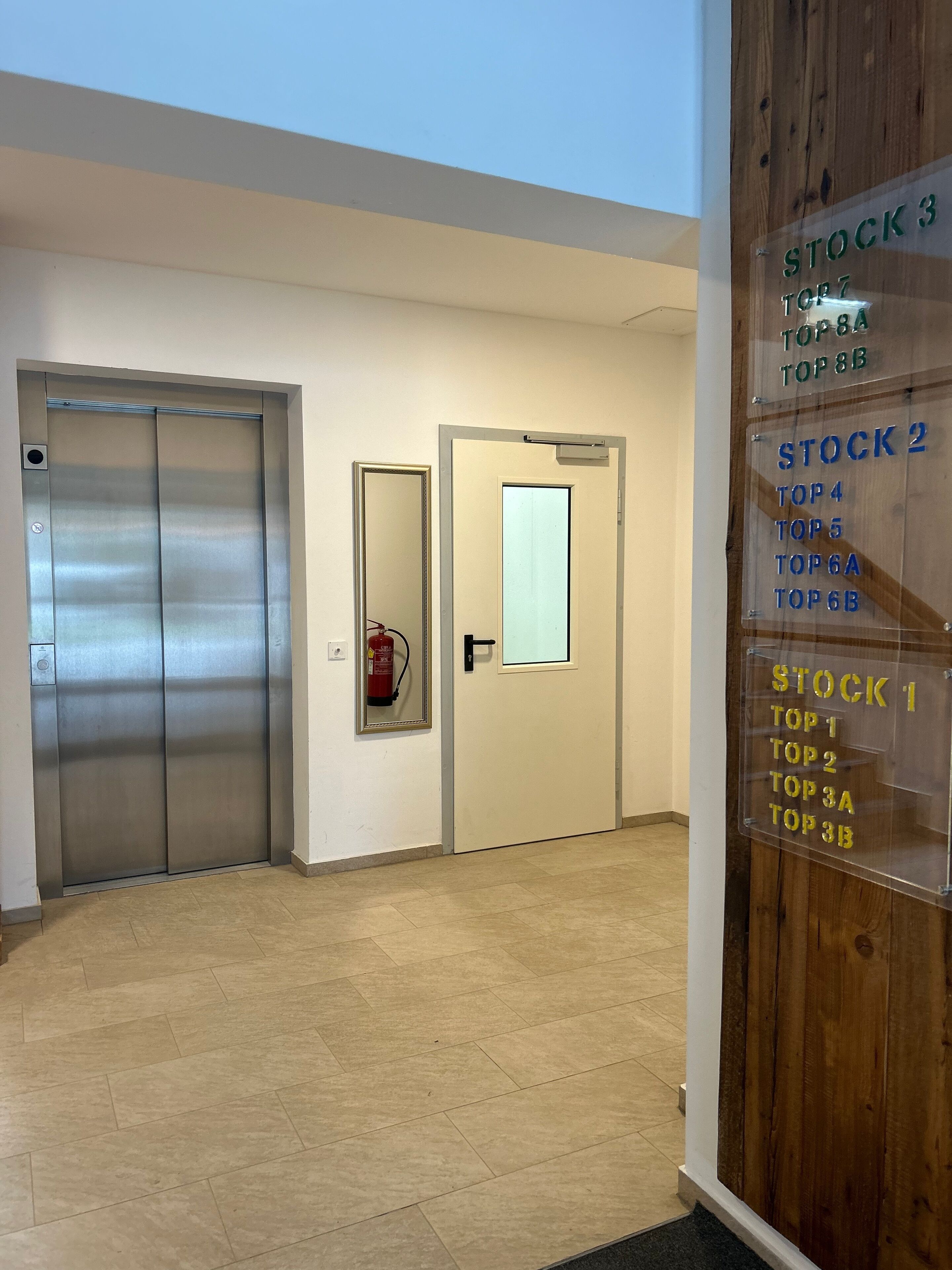 A hallway with an elevator, a door with a mirror, and a wooden panel with stock rankings.