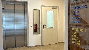 A hallway with an elevator, a door with a mirror, and a wooden panel with stock rankings.