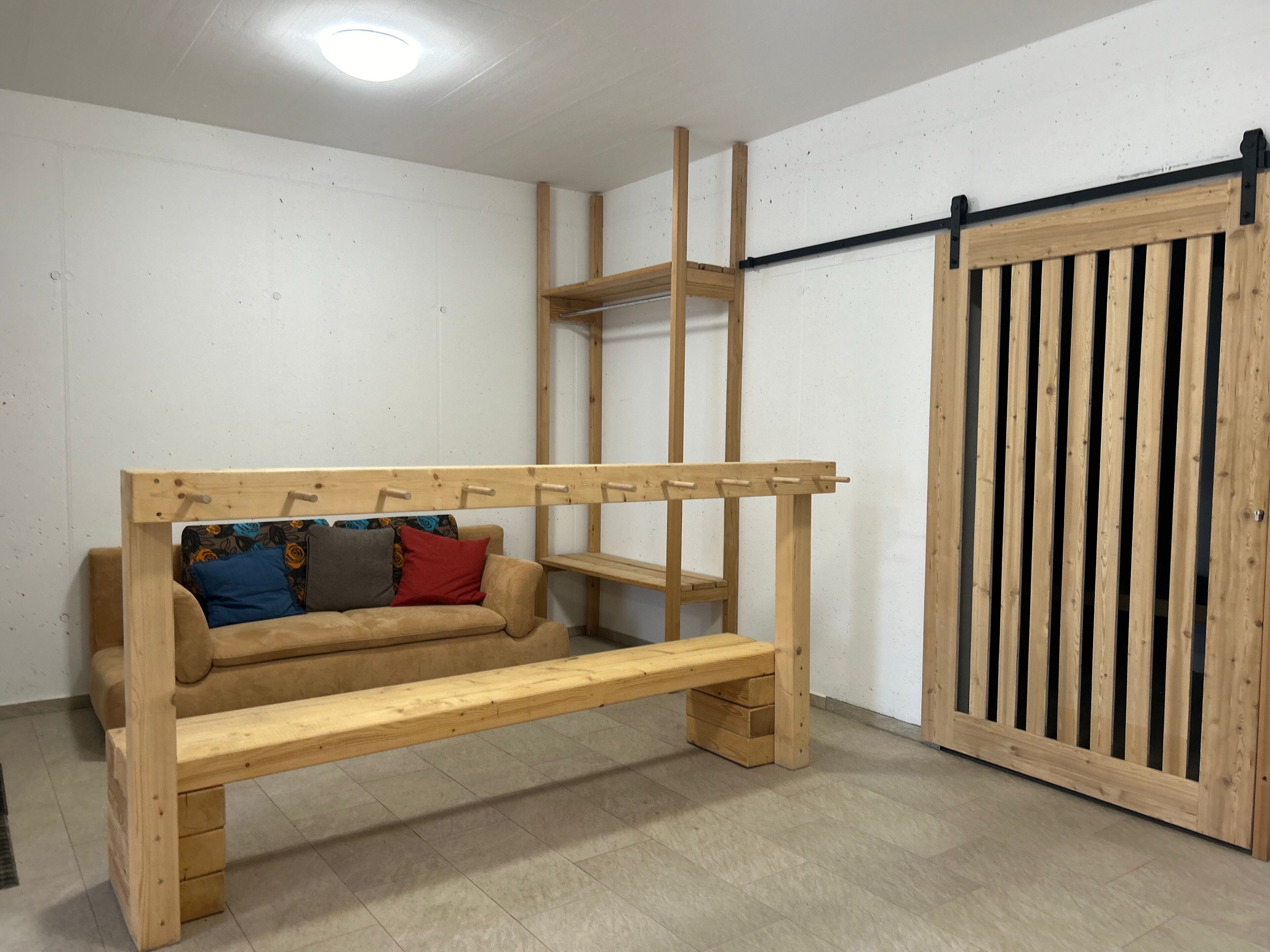 Une pièce avec un banc en bois, un canapé agrémenté de coussins colorés et une porte coulissante à lames verticales.