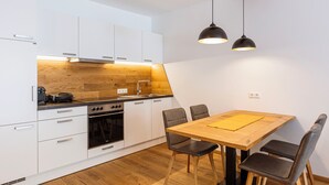 A modern kitchen with white cabinets, a wooden countertop, a built-in oven, and a dining table with chairs. - Turrach Suites 410 by ALPS RESORTS (Stadl-Predlitz)