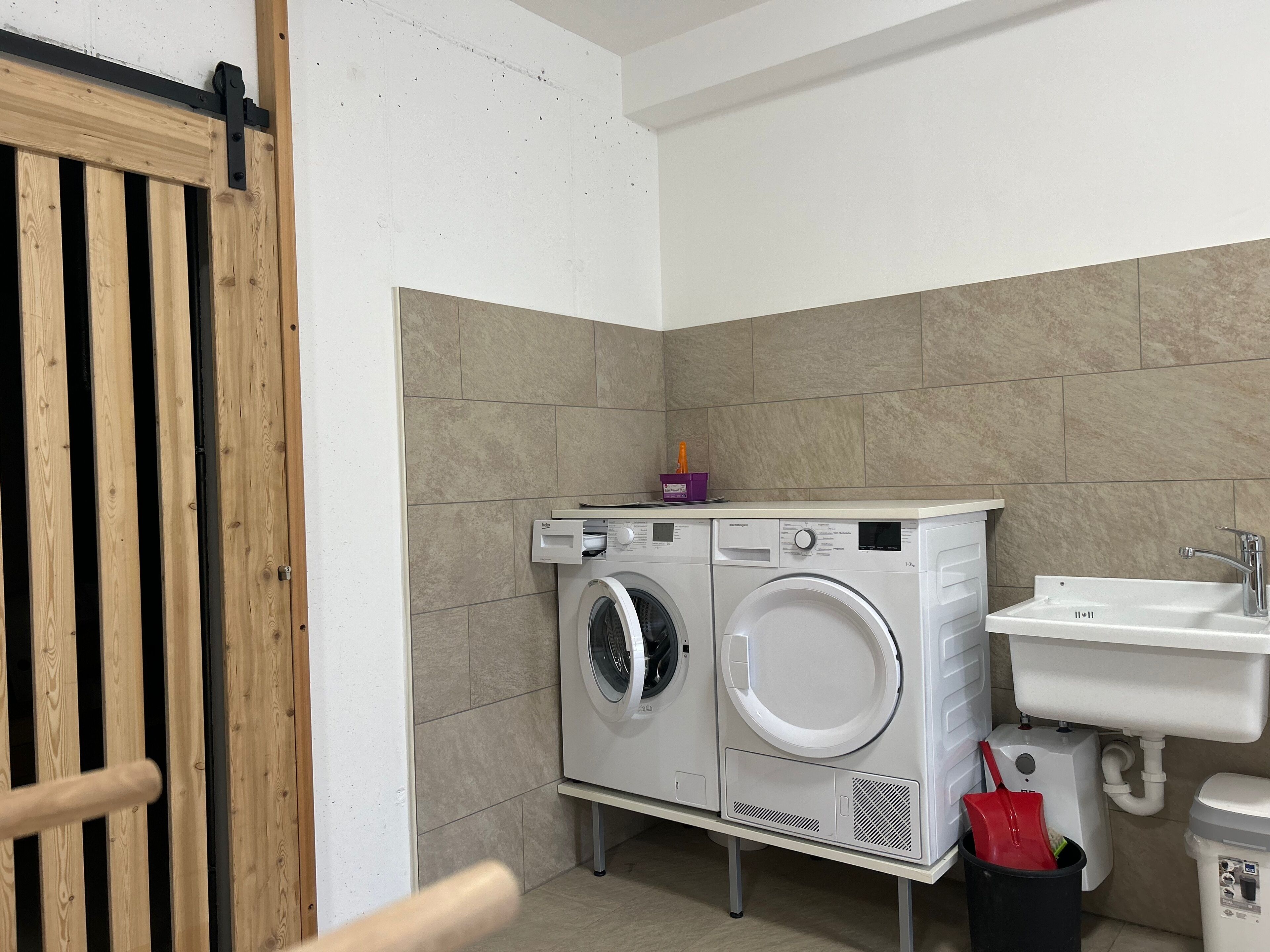 A compact laundry area with two front-loading washing machines, a sink, and a wooden door.
