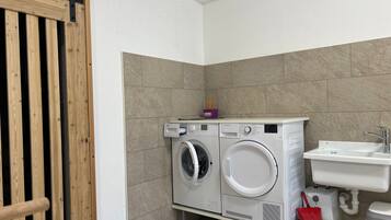 A compact laundry area with two front-loading washing machines, a sink, and a wooden door.