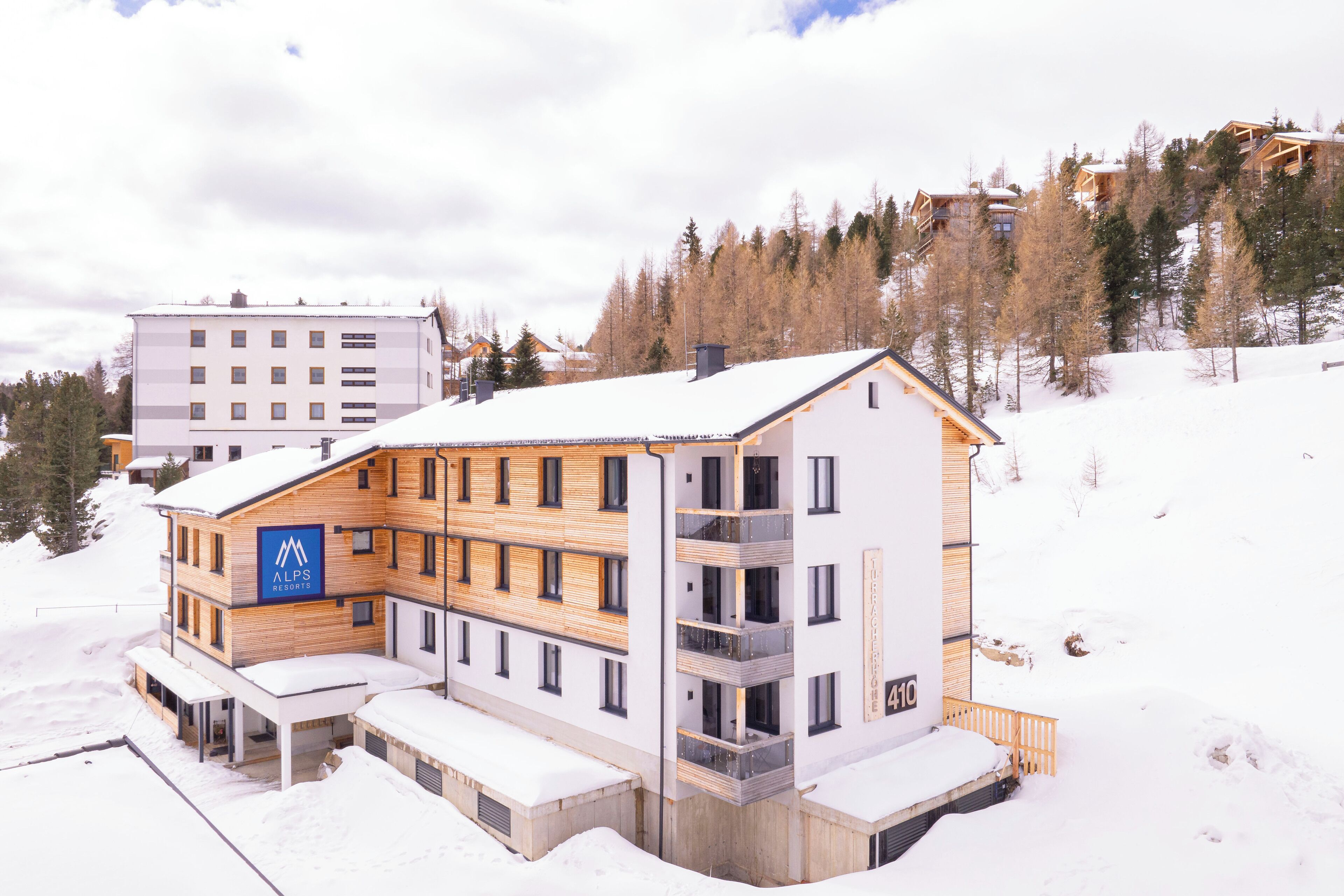 A modern hotel with a wooden facade, multiple balconies, and a snow-covered landscape.