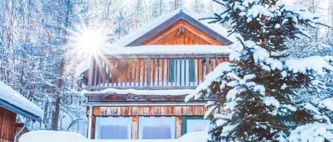 Una cabaña de madera con balcón, rodeada de árboles cubiertos de nieve.