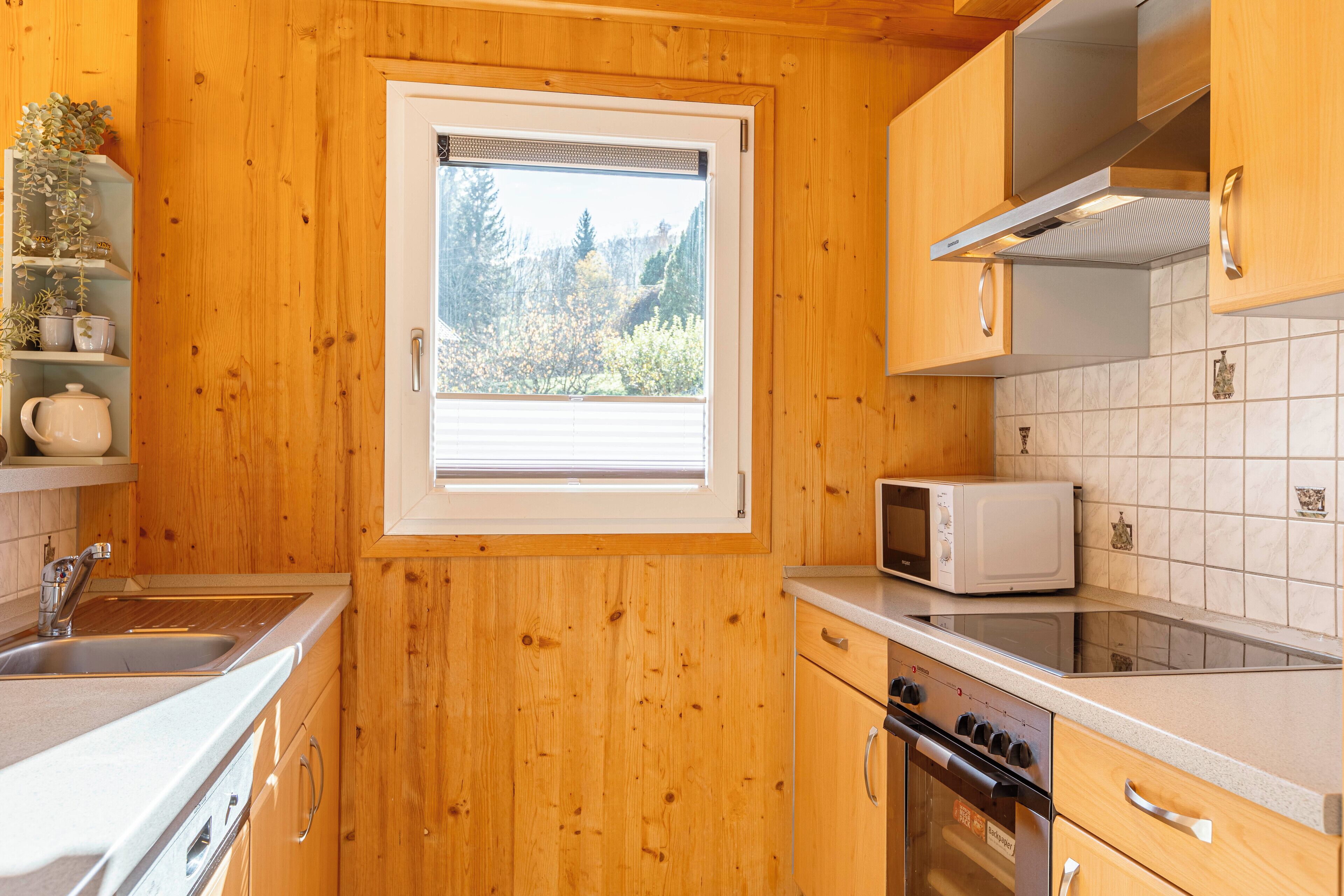 A kitchen with wooden cabinets, a microwave, a stove, and a window with a view of trees.